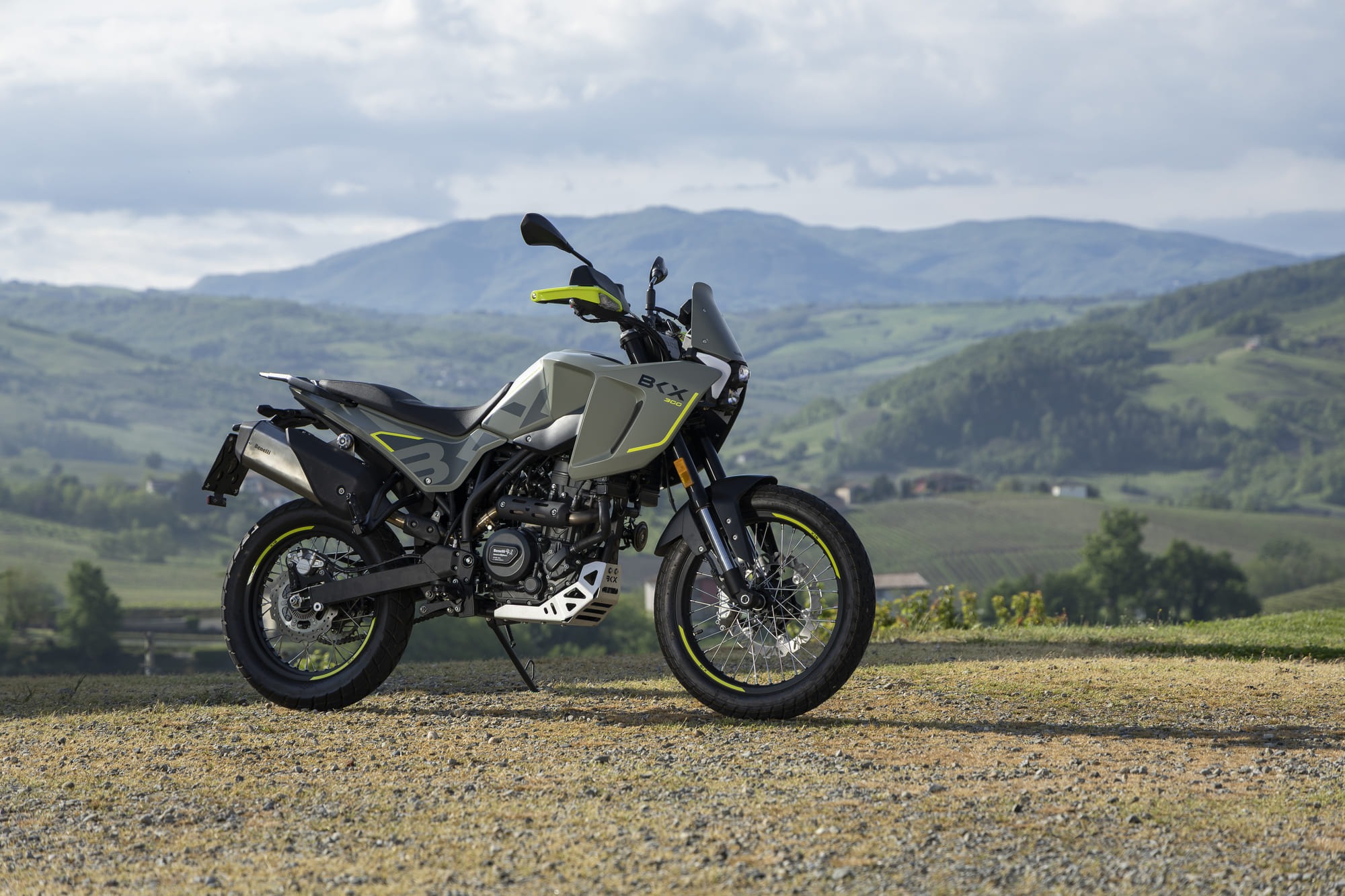 Benelli-bkx-300 3 - AutoBike Adventure motorcycle parked on a gravel road with rolling green hills and a cloudy sky in the background. - AutoBike