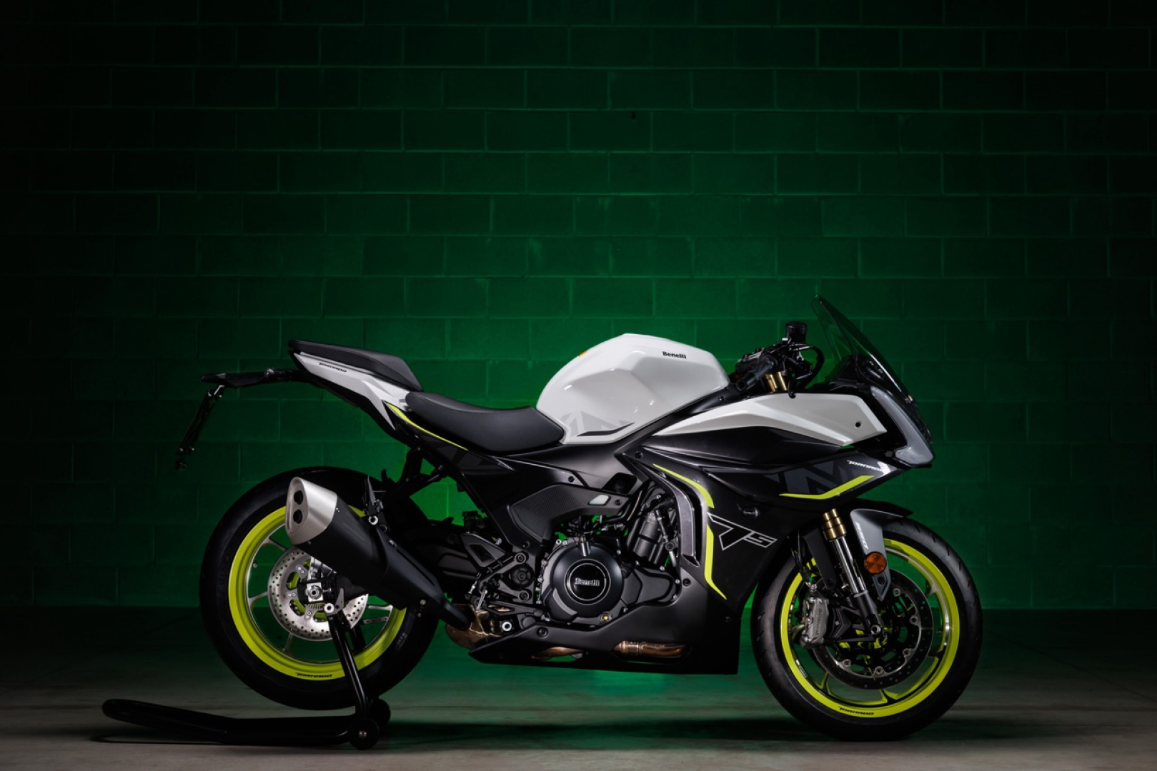 Benelli-tornado-550 1 - AutoBike White and black sport motorcycle with neon yellow rims and accents, parked indoors against a dark green brick wall. - AutoBike