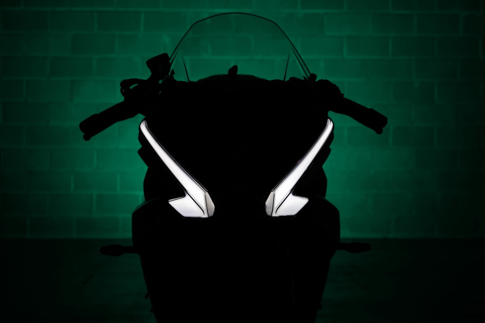 Benelli-tornado-550 2 - AutoBike Silhouette of a sport motorcycle head-on in a dark room, with green backlighting and glowing headlights. - AutoBike