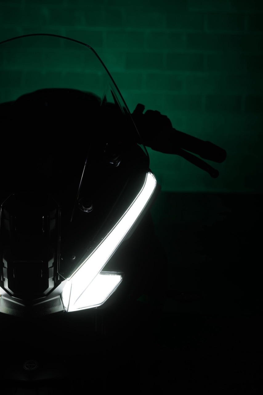 Benelli-tornado-550 5 - AutoBike Front view of a motorcycle with a bright white LED headlight, silhouetted rider stretched along the bike against a green wall. - AutoBike