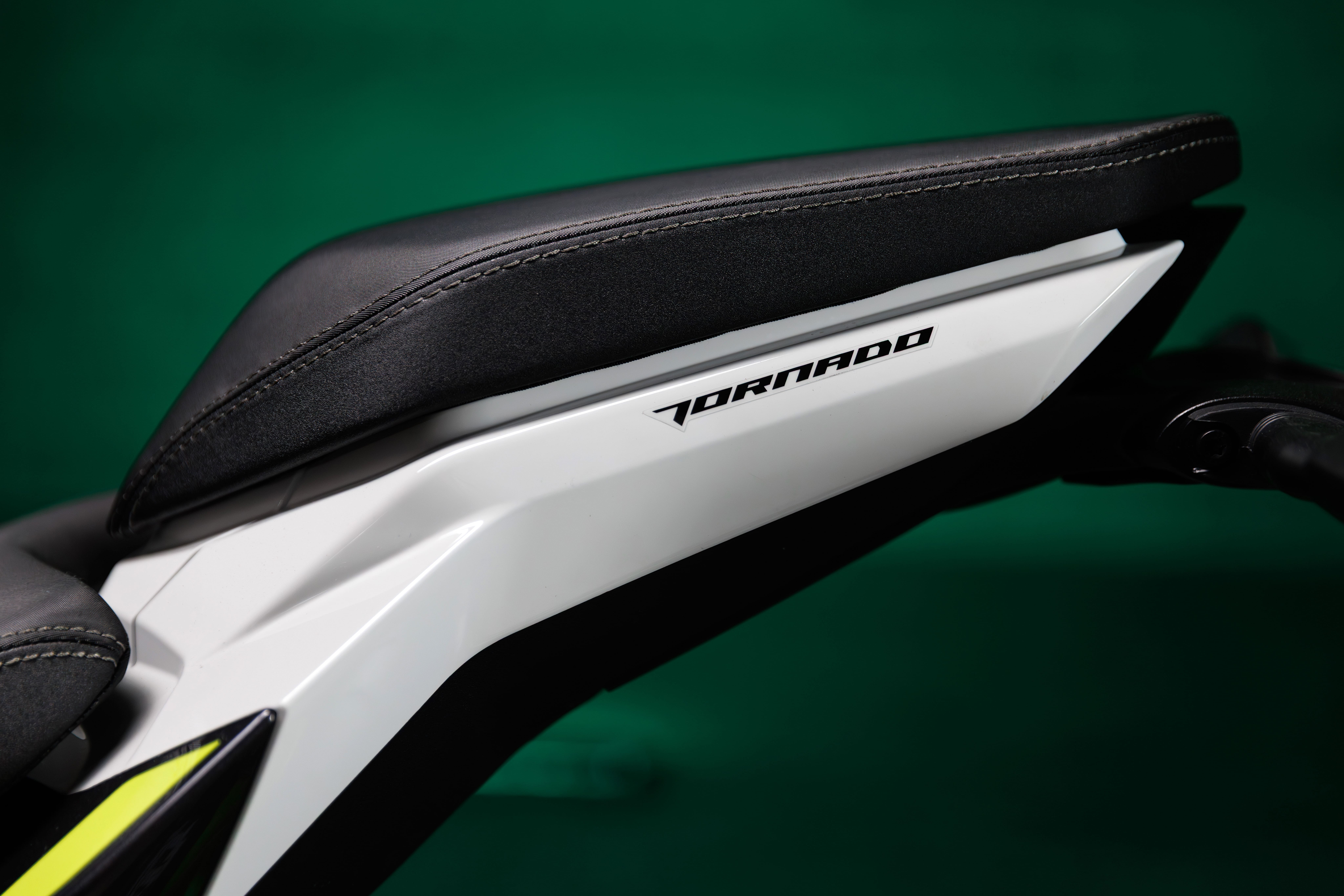 Benelli-tornado-550 - AutoBike Close-up of a white motorcycle frame with a black stitched seat and visible Tornado branding against a green background. - AutoBike