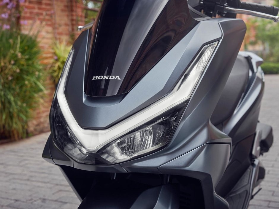 honda-pcx-125- 23 - AutoBike Close-up of a modern Honda scooter's front, showing angular LED headlight, metallic gray panels, and the Honda emblem. - AutoBike