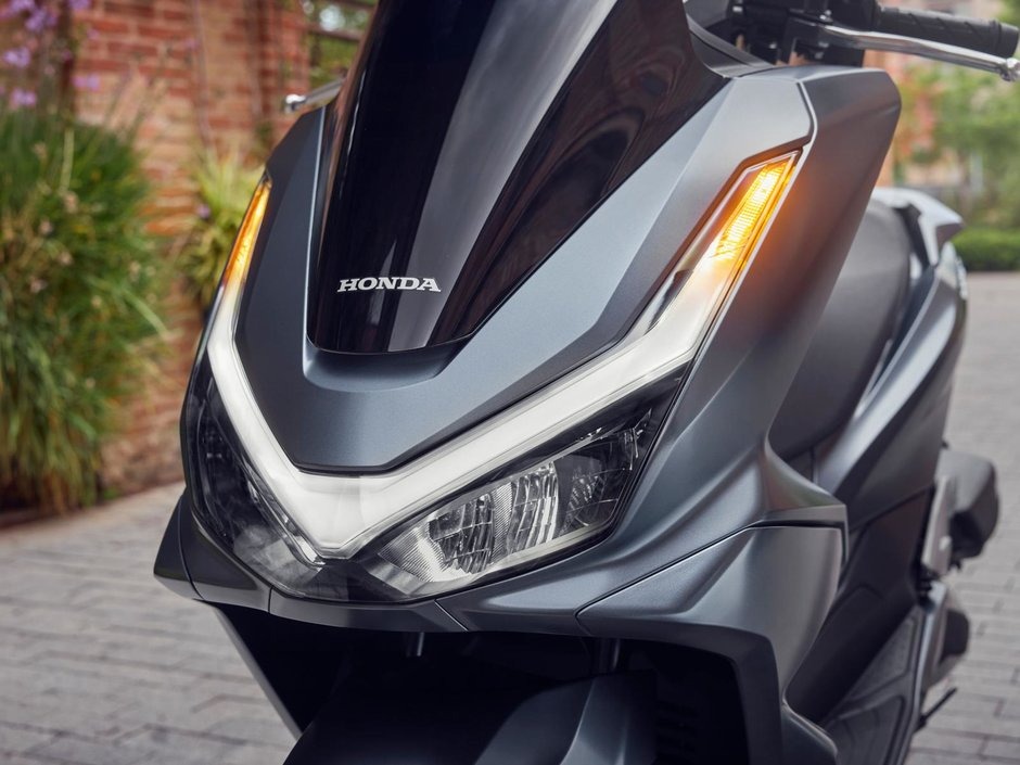 honda-pcx-125- 24 - AutoBike Front view of a Honda scooter with illuminated turn signals and sharp LED headlight design. - AutoBike