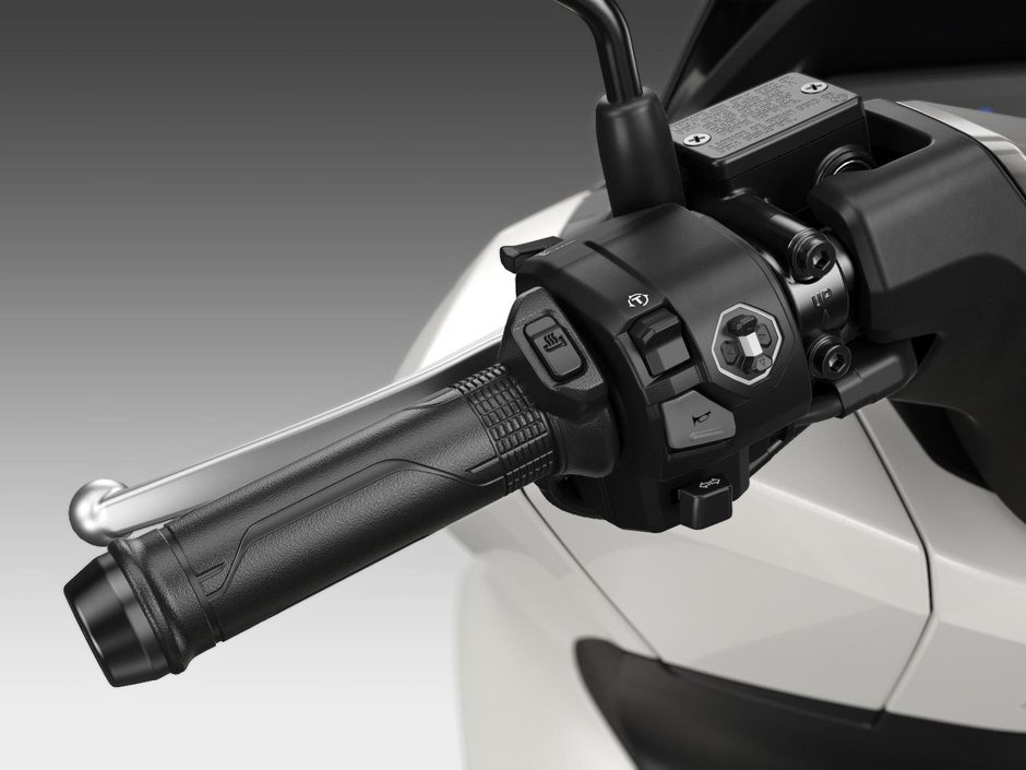honda-pcx-125- 28 - AutoBike Close-up of a motorcycle handlebar cluster with switchgear (horn, indicators, lights) and textured throttle grip on a white bike - AutoBike