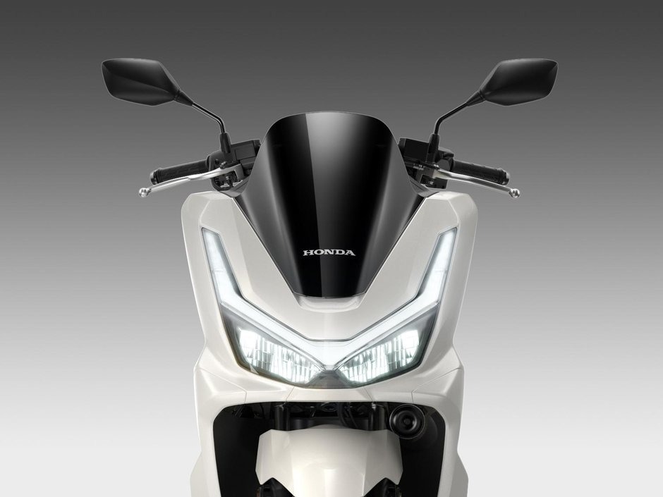 honda-pcx-125- 30 - AutoBike Front view of a white Honda scooter with a black windscreen and V-shaped dual headlights, LED daytime running lights clearly visible - AutoBike