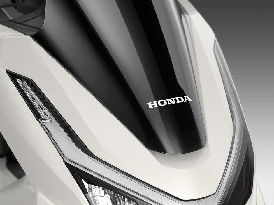 honda-pcx-125- 31 - AutoBike Close-up of a white Honda motorcycle front with a glossy black central panel and the Honda logo nearby. - AutoBike