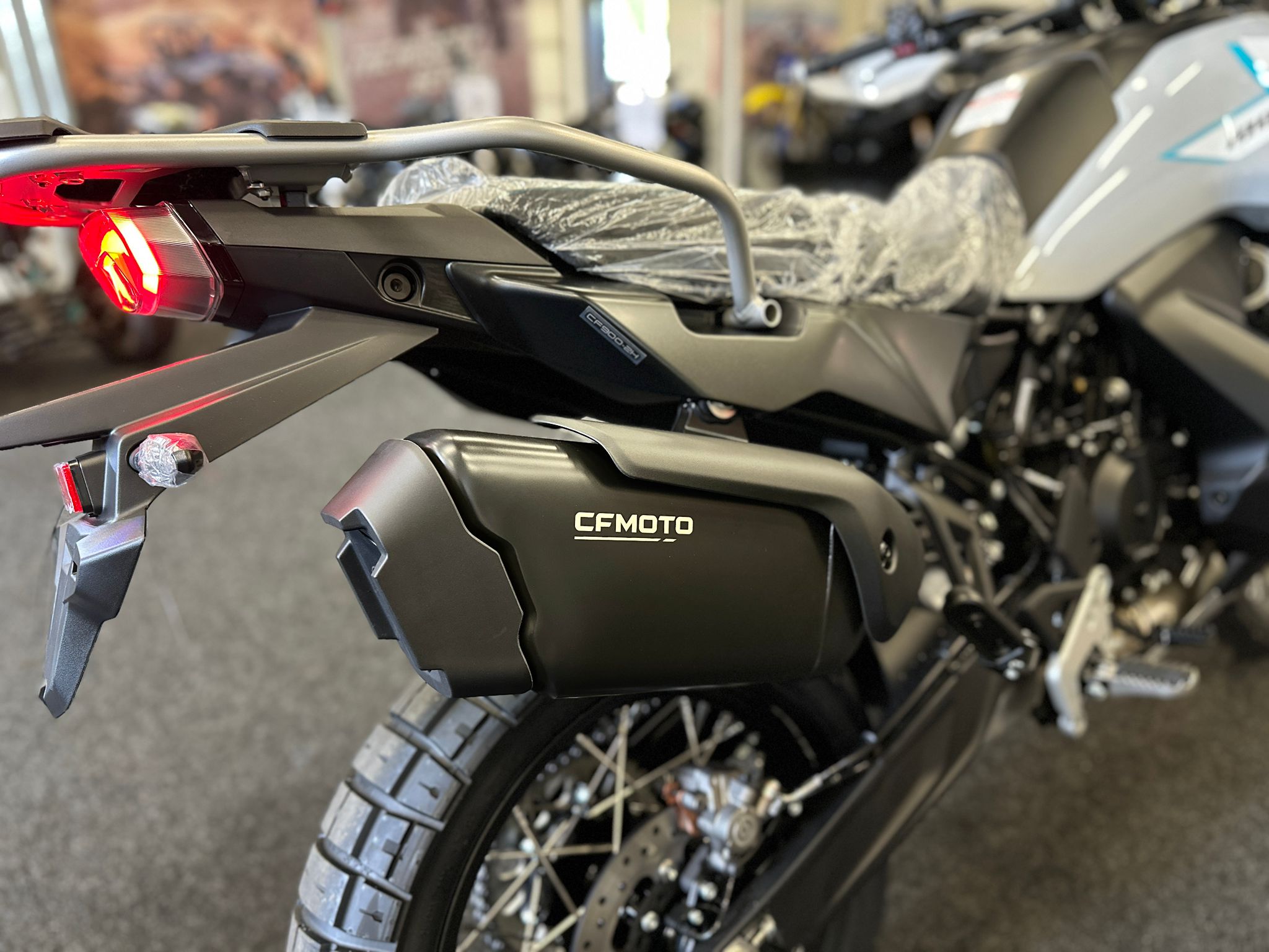 CFMOTO-1000-MT-X-1-18 at 203524 - AutoBike Close-up of the rear end of a CFmoto motorcycle, showing the red taillight, rear fender, and luggage rack with protective wrapping. - AutoBike