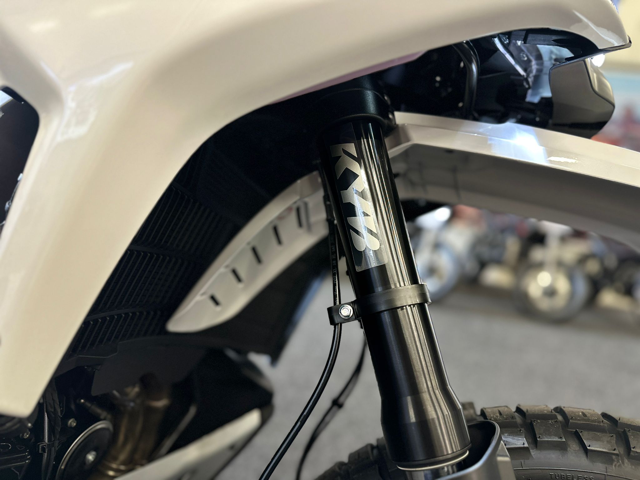 CFMOTO-1000-MT-X-1-18 at 203525 1 - AutoBike Close-up of a white mountain bike's front suspension fork with a black stanchion and a visible cable along the fork leg. - AutoBike