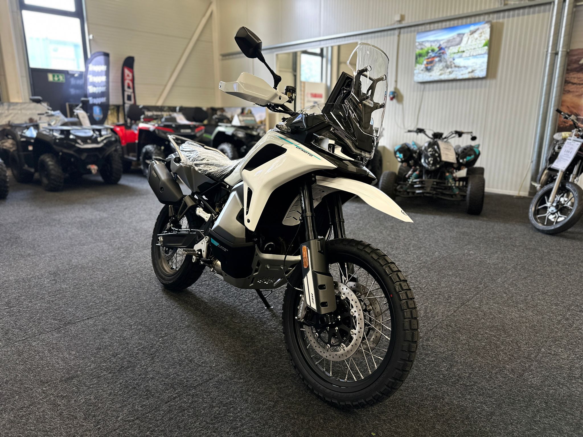 CFMOTO-1000-MT-X-1-18 at 203526 - AutoBike White adventure motorcycle on display in a showroom with other ATVs visible in the background - AutoBike