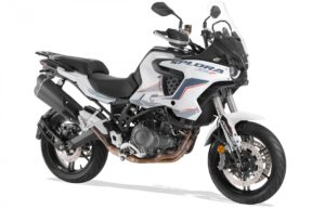 Adventure motorcycle with white and black body, red/blue decals, shown from the side with a clear windscreen and dual exhausts.