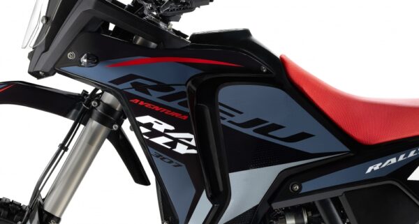 Close-up of a black motorcycle with blue side panels, red seat, and front suspension in view, showing an 'Adventure' graphic on the body. - AutoBike