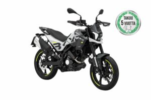Side view of a gray and black motorcycle with neon-yellow rim accents and a circular 'TAKUU 5 VUOTTA' warranty badge on the right side of the image.