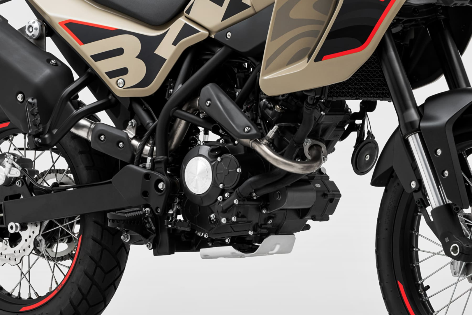 Benelli-bkx-125-s 2 - AutoBike Close-up of a rugged adventure motorcycle's engine and exhaust system, tan body panels with red accents, black frame, and front fork visible against a light background. - AutoBike