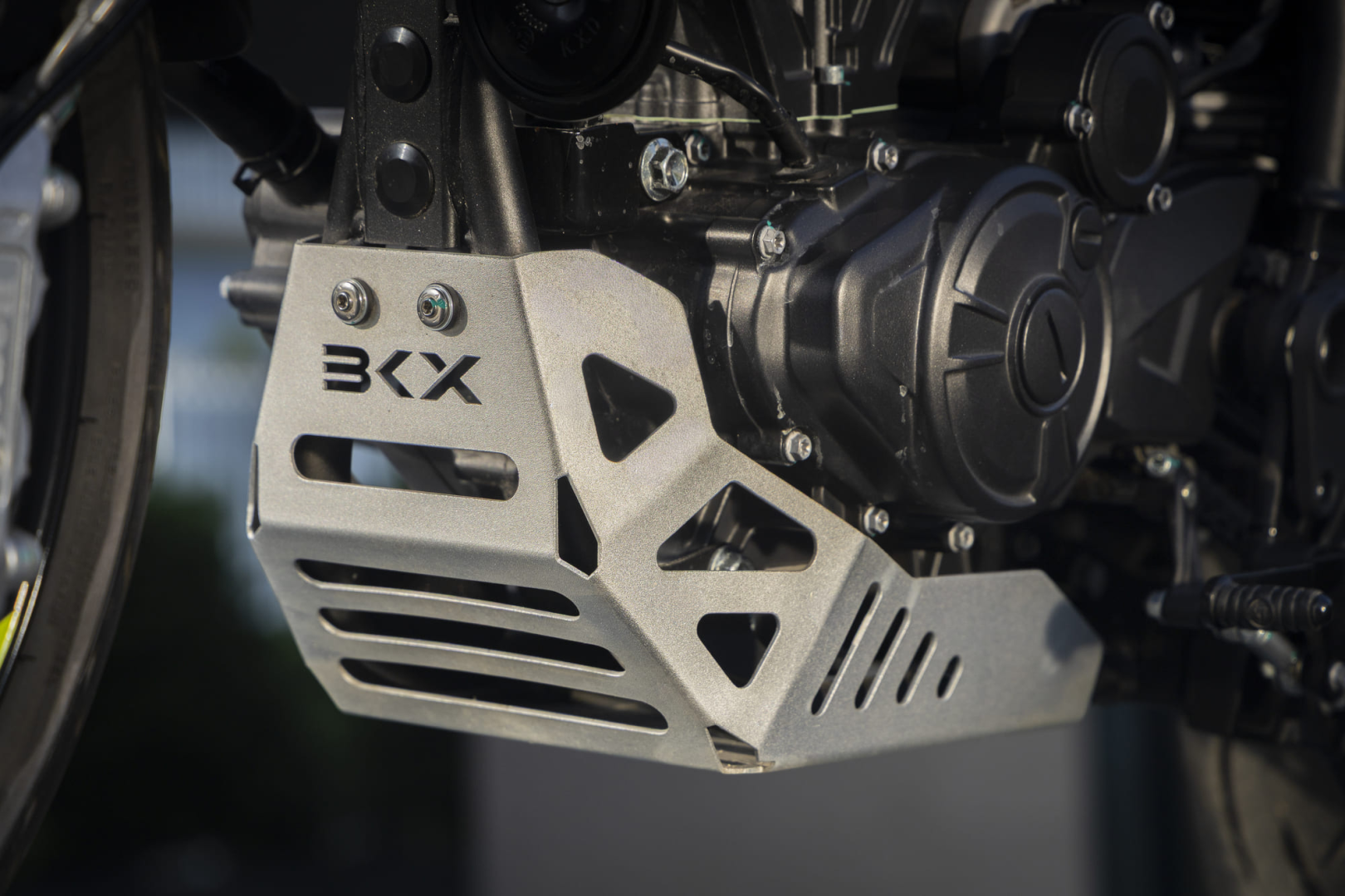 Benelli-bkx-125-s 4 - AutoBike Close-up of a metal motorcycle skid plate with BKX branding and geometric cutouts over the engine casing - AutoBike
