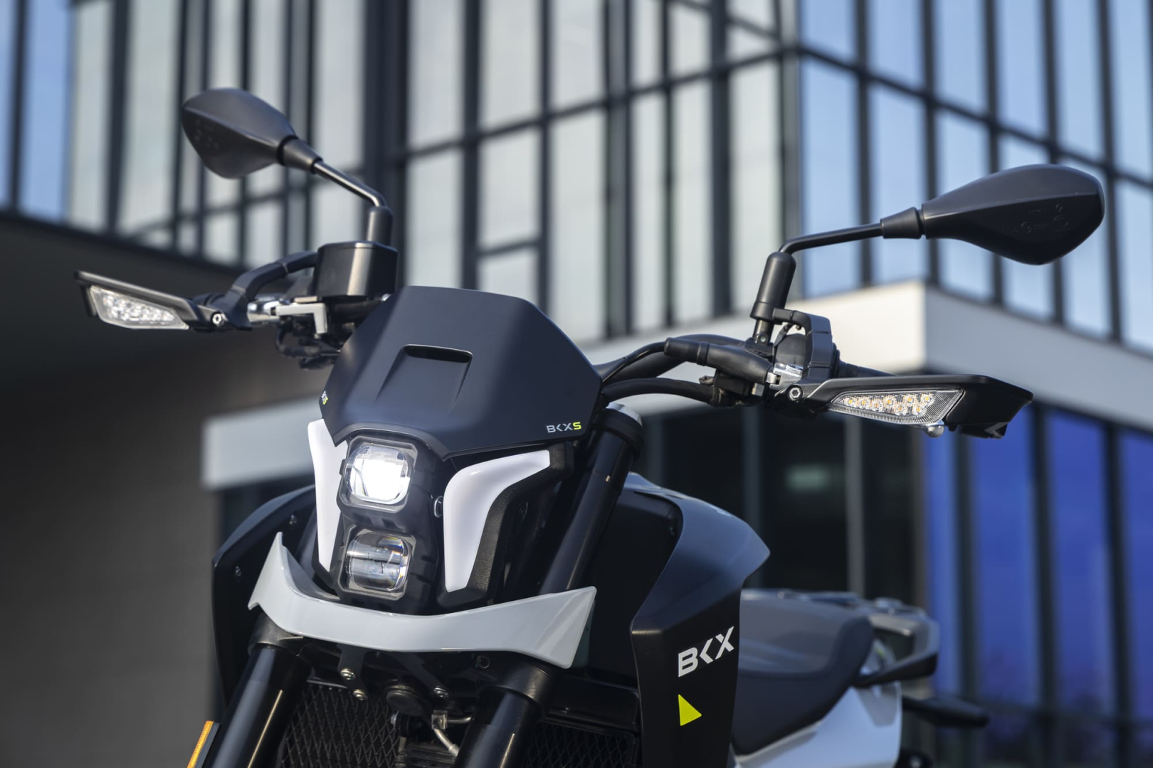 Benelli-bkx-125-s - AutoBike Front view of a black motorcycle with dual headlights and side mirrors, modern glass building in the background. - AutoBike