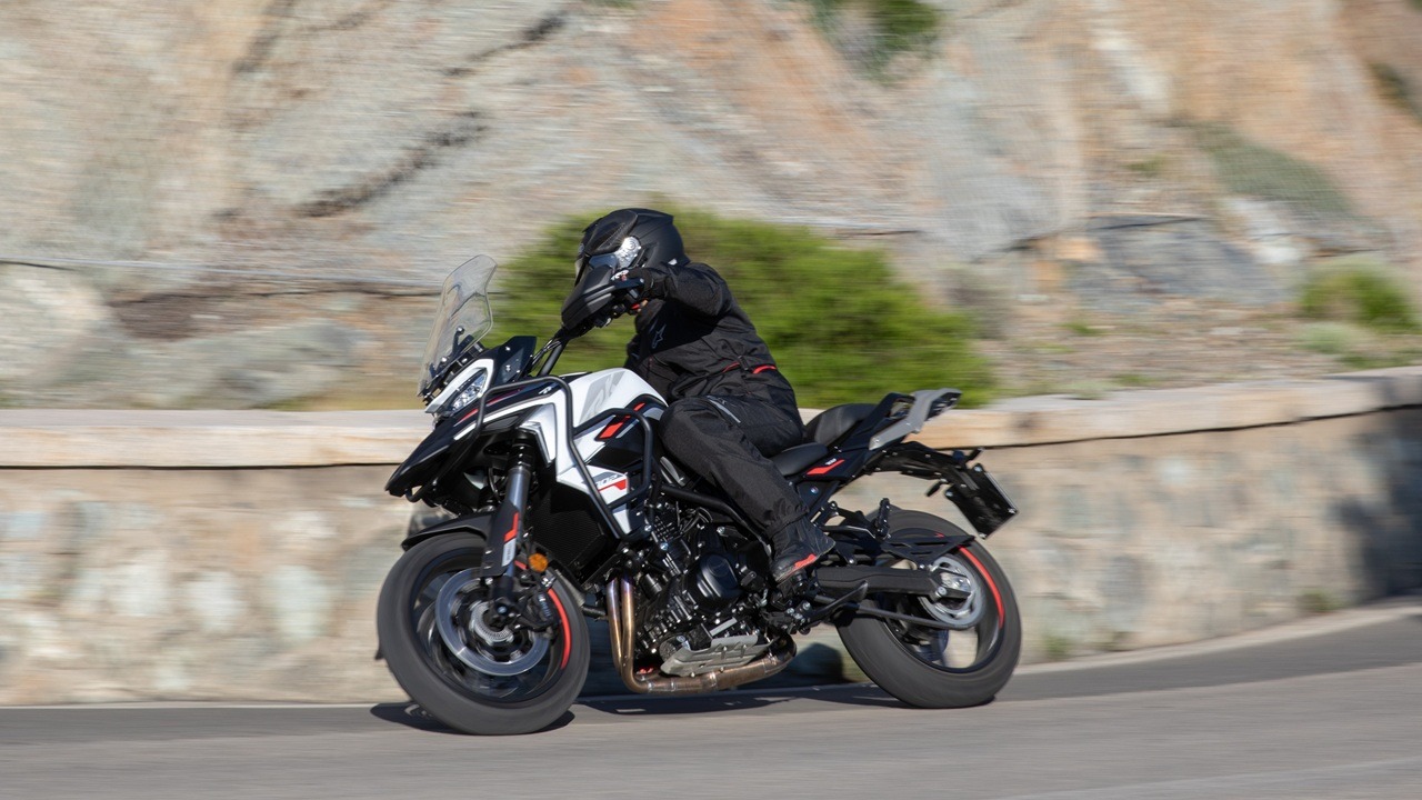 Benelli-trk-702 3 - AutoBike Motorcyclist wearing full protective gear leaning into a turn on a white-and-black sport motorcycle on a winding mountain road. - AutoBike