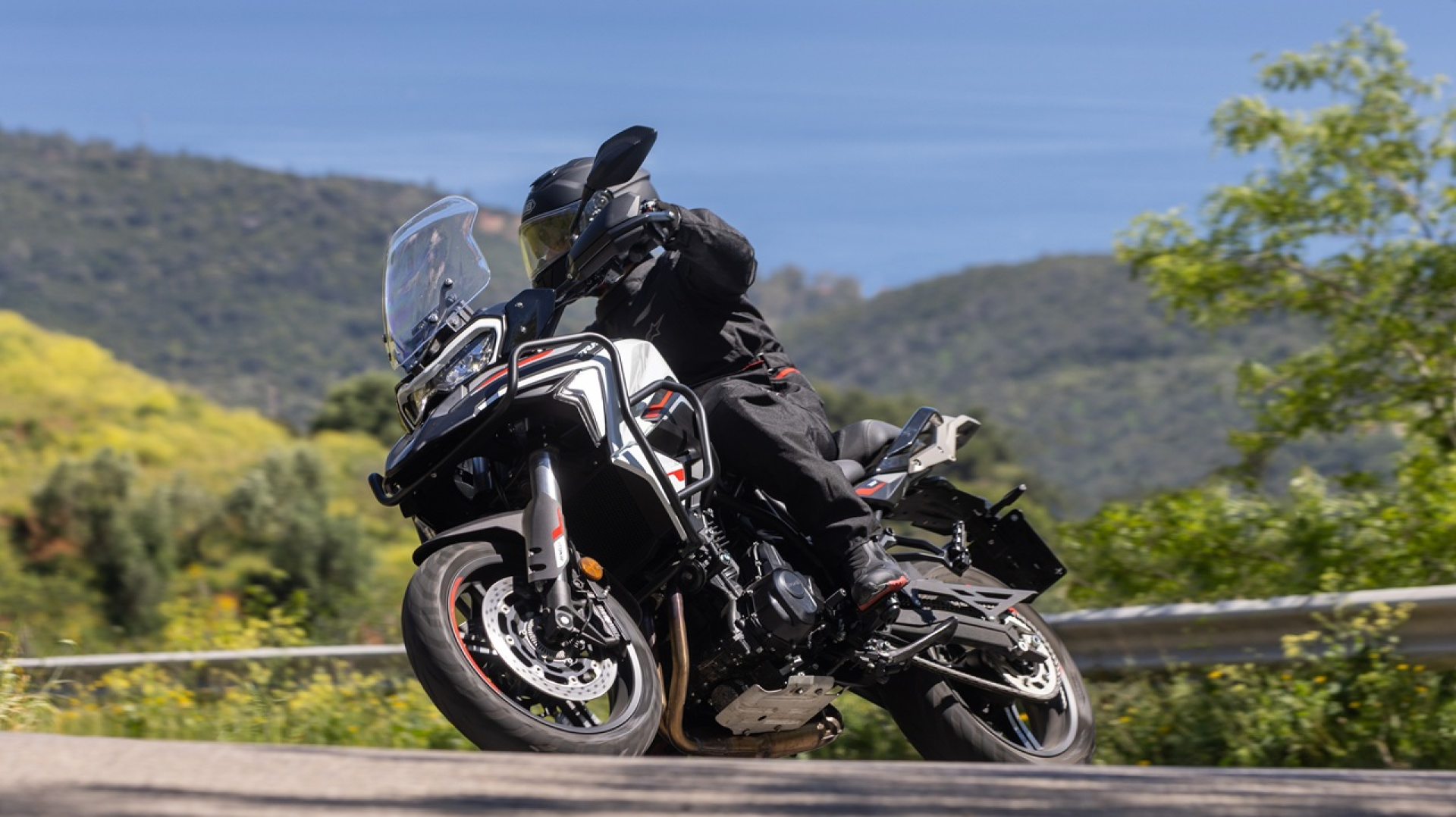 Benelli-trk-702 3 - AutoBike Motorcyclist in black gear leaning into a curve on a sport motorcycle on a sunny mountain road. - AutoBike