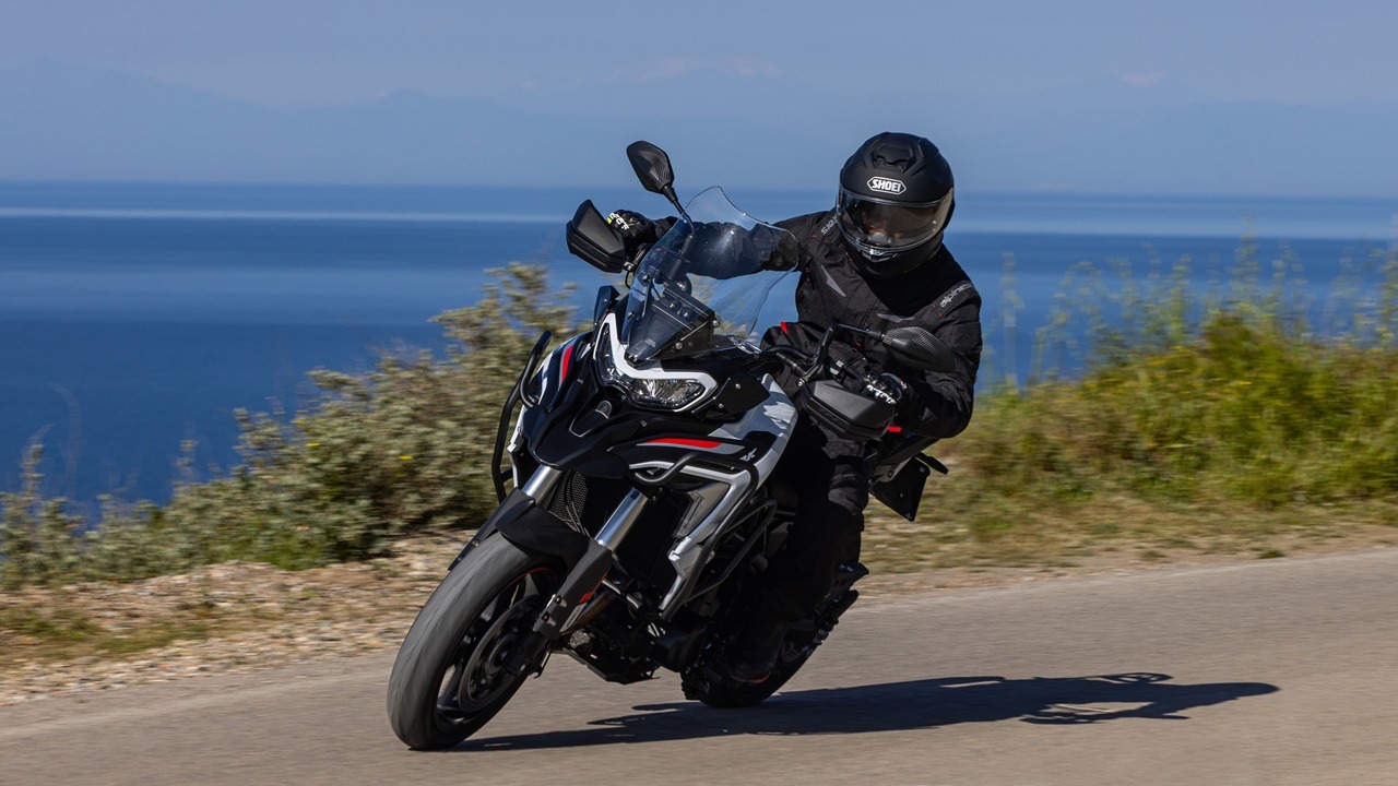 Benelli-trk-702 7 - AutoBike Motorcyclist in black gear and helmet leaning into a curve on a coastal road with the blue sea in the background. - AutoBike
