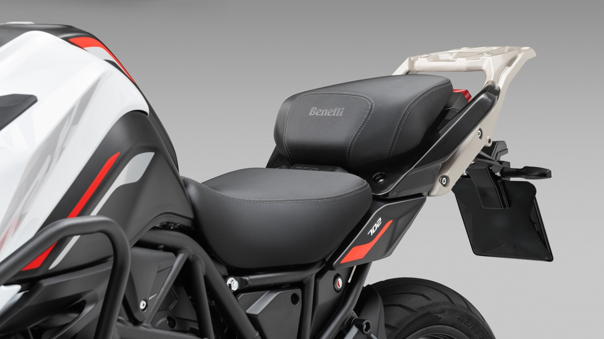 Benelli-trk-702 - AutoBike Close-up of a Benelli motorcycle seat and rear section with black stitching and red accents. - AutoBike