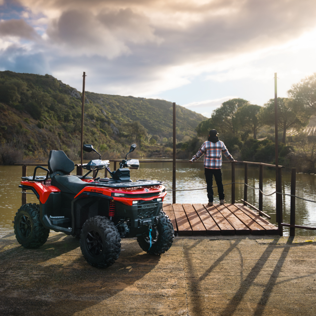 CFMOTO_CFORCE-C5_Outdoor_17-1030x1030 - AutoBike Red ATV parked on a wooden dock beside a lake, with a person in a plaid shirt looking out over the water. - AutoBike