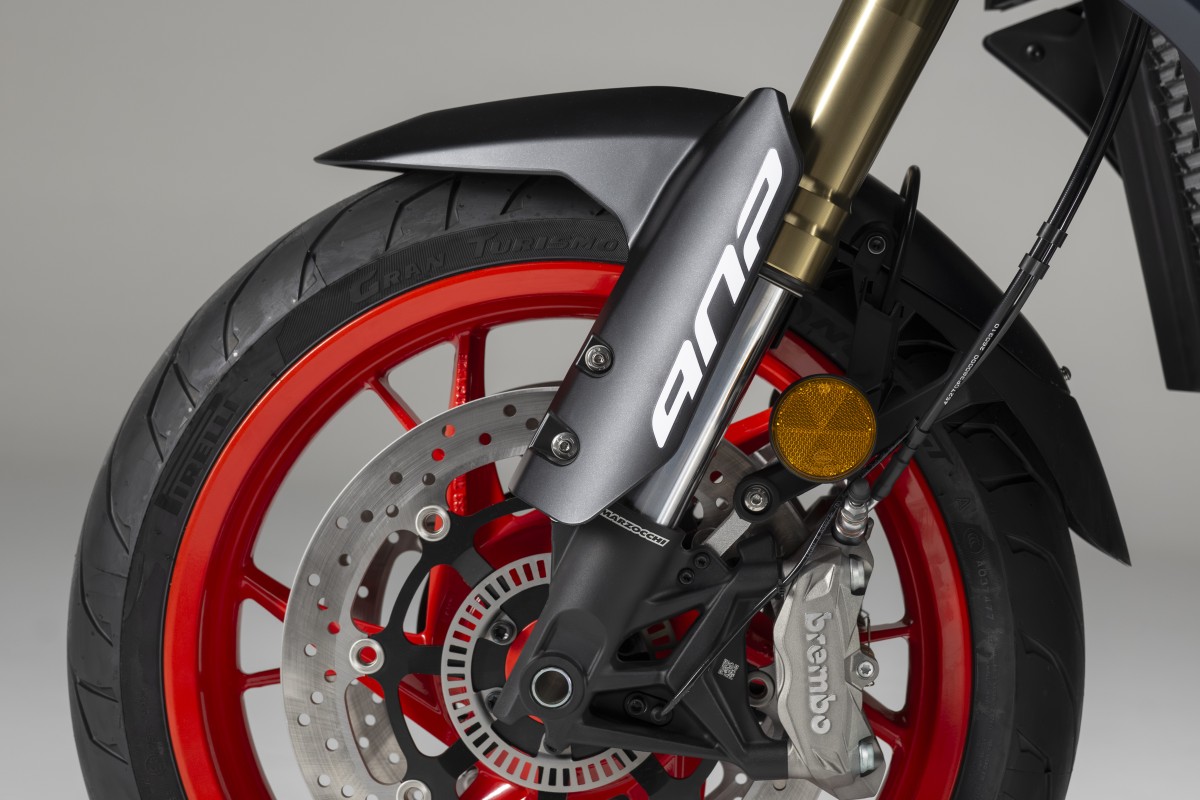 Benelli-trk902-stradale-brembo - AutoBike Front wheel of a sport motorcycle with a red alloy rim, drilled brake disc, Brembo caliper, and gold inverted fork. - AutoBike