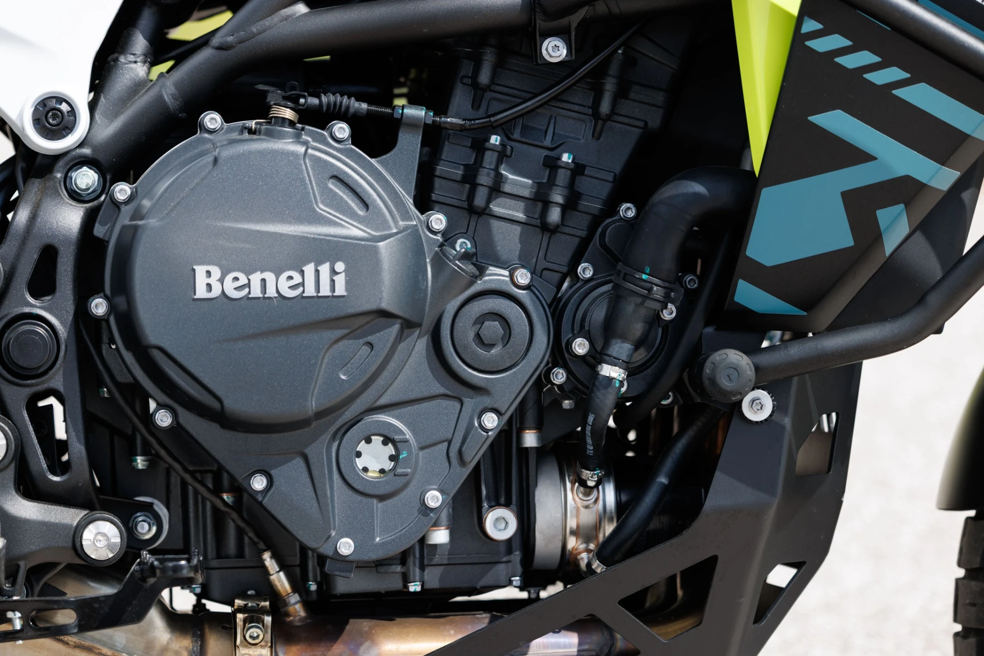 TRK902_Xplorer_044-5 - AutoBike Close-up of a Benelli motorcycle engine and frame, showing the gray engine cover and surrounding hoses and bolts. - AutoBike