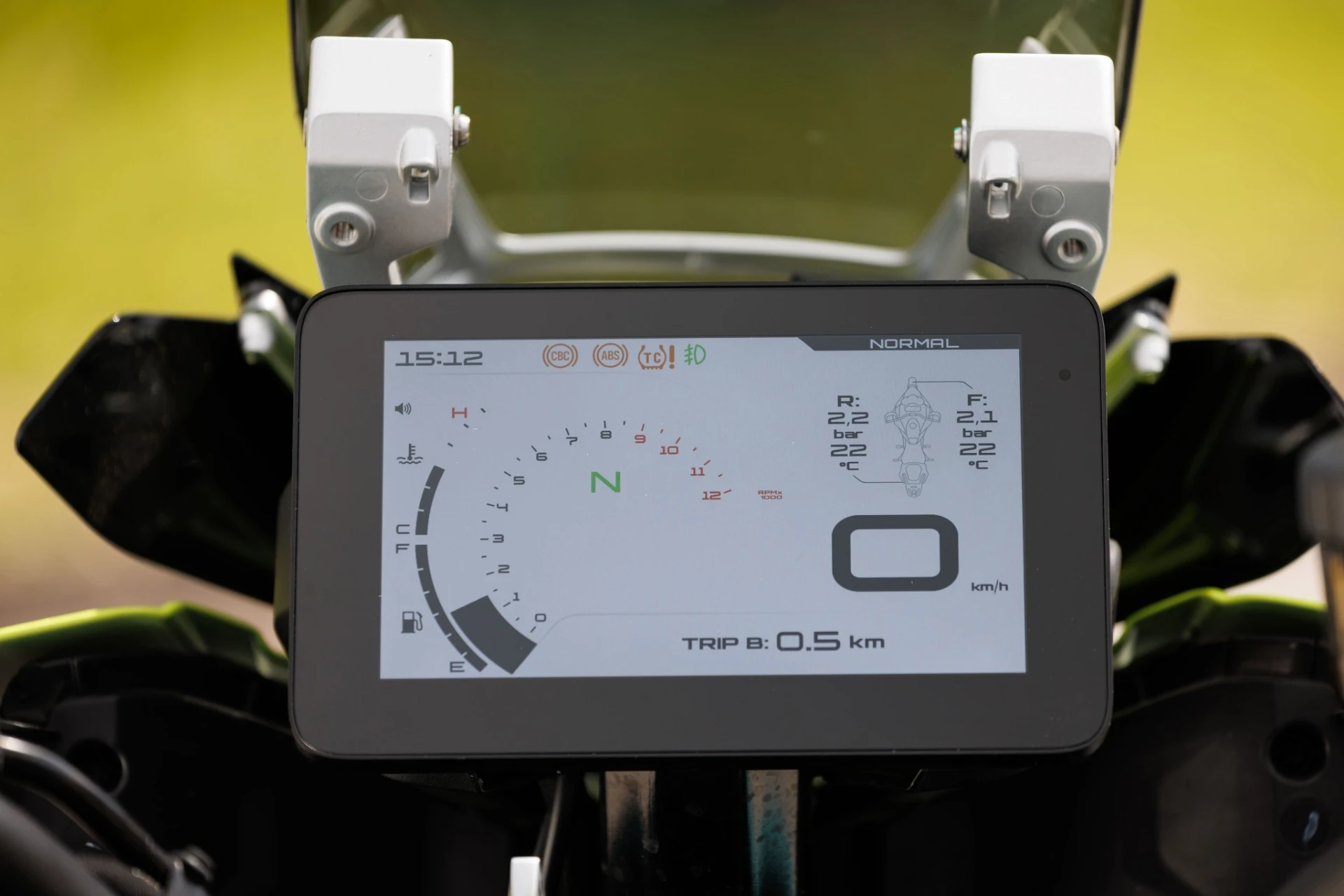 TRK902_Xplorer_096-74 - AutoBike Close-up of a motorcycle cockpit with a digital gauge cluster showing time 15:12, gear N, fuel gauge, and trip readout 0.5 km. - AutoBike