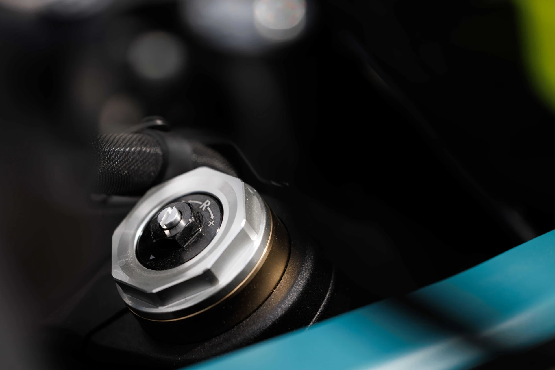 trk902_xplorer_102_optimized 1 - AutoBike Close-up of a metallic adjustment dial with a knurled edge on a dark motorcycle component, against a black background and teal body panel. - AutoBike