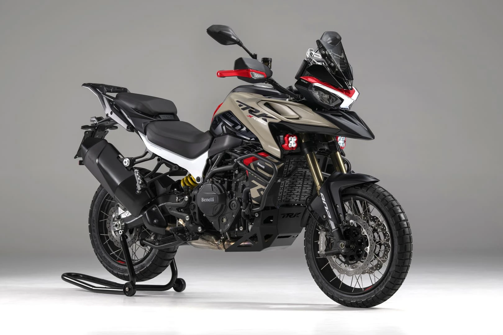 trk902_xplorer_colors_34_dune-sea - AutoBike Side view of a modern adventure motorcycle on a rear stand, beige and black body with red accents and prominent windscreen. - AutoBike