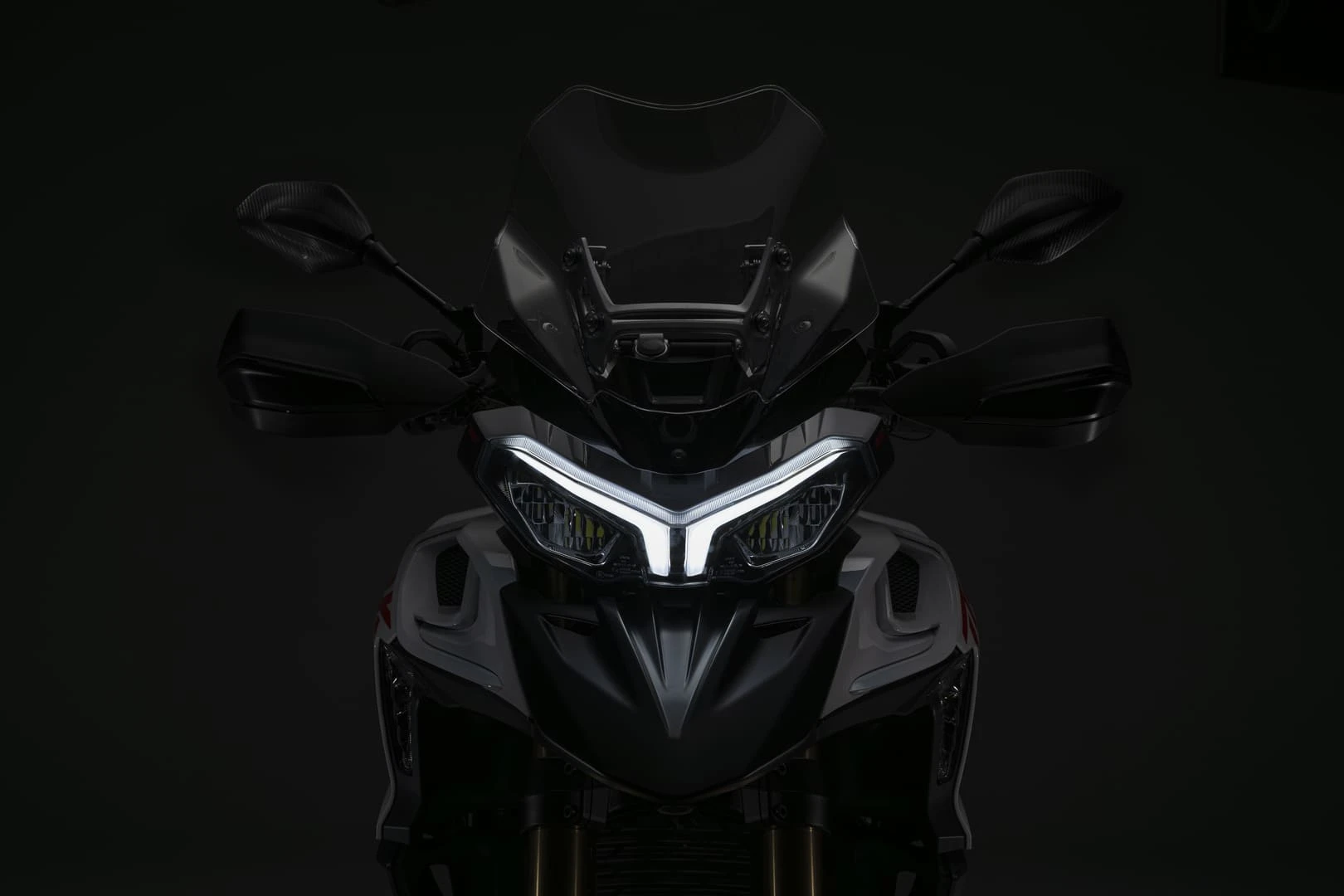trk902stradale_10 - AutoBike Front view of a dark motorcycle with illuminated angular LED headlights against a black background. - AutoBike