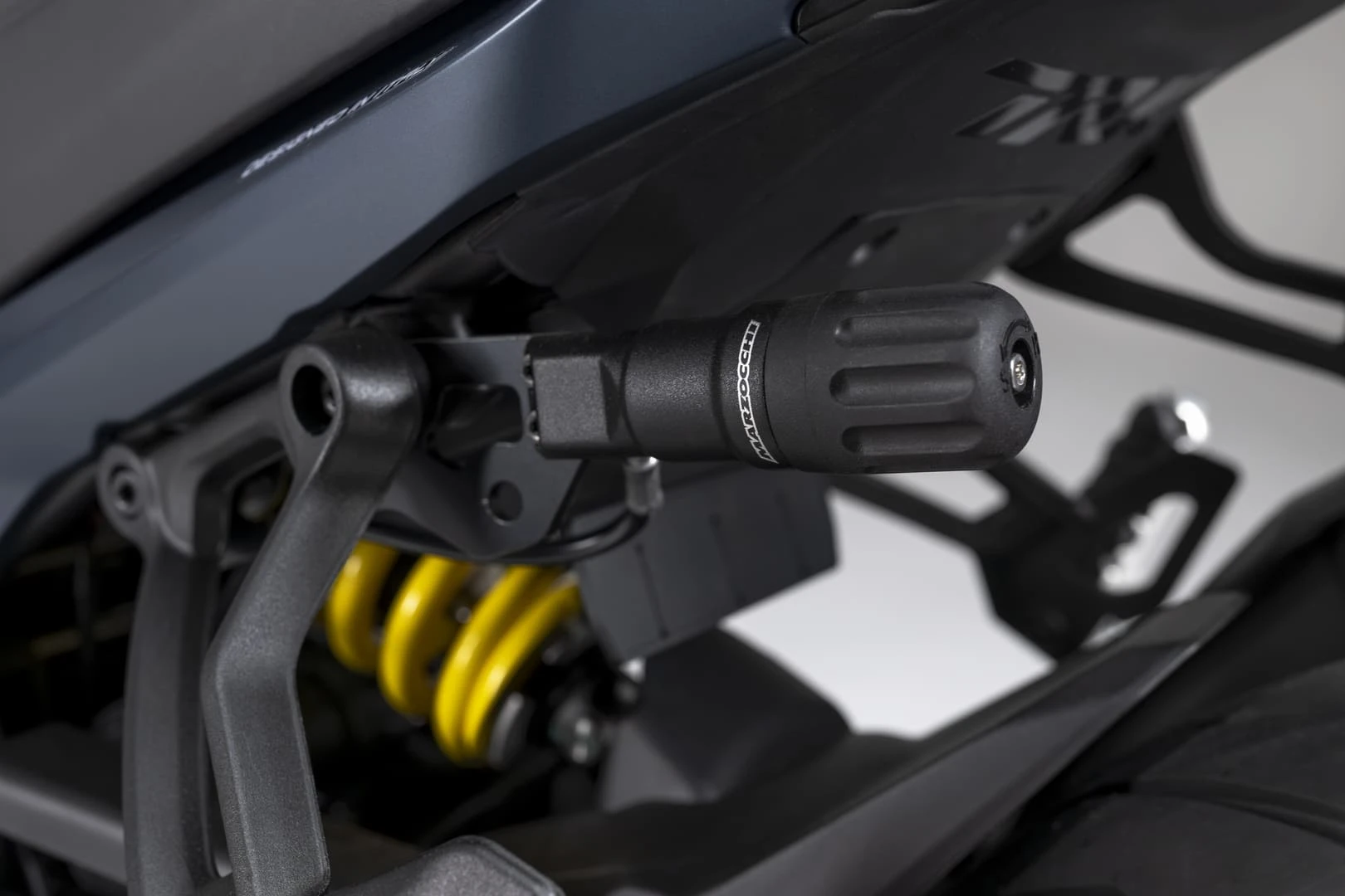 trk902stradale_26 - AutoBike Close-up of a black, ribbed, cylindrical adjustment knob mounted on a motorcycle's rear suspension, with a yellow coil spring visible nearby. - AutoBike