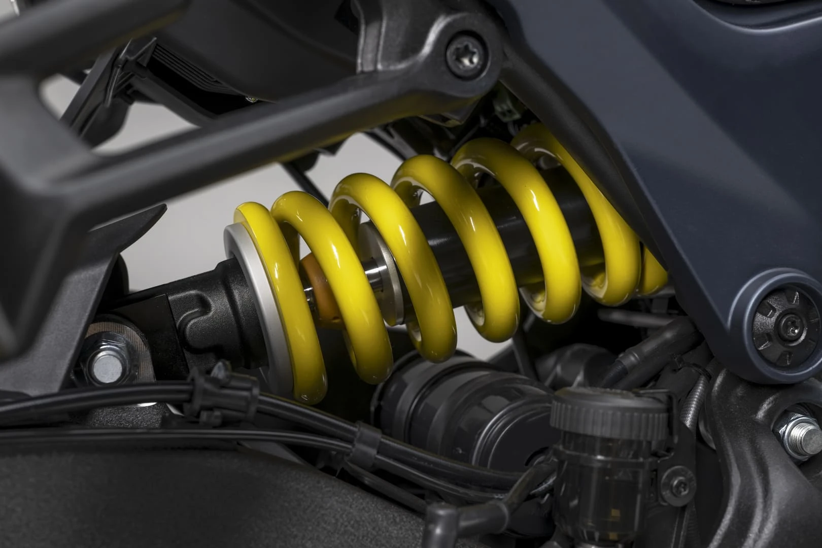 trk902stradale_27 - AutoBike Close-up of a bright yellow coil spring shock absorber in a motorcycle's rear suspension, with metal mounting hardware nearby. - AutoBike