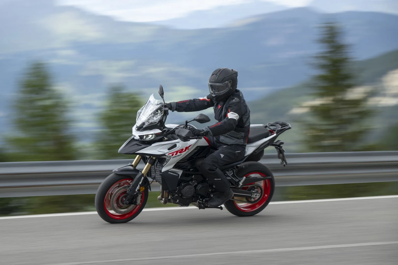 trk902stradale_action_13 - AutoBike Motorcyclist wearing full gear riding a white motorcycle with red rims on a highway, blurred mountain scenery in the background - AutoBike
