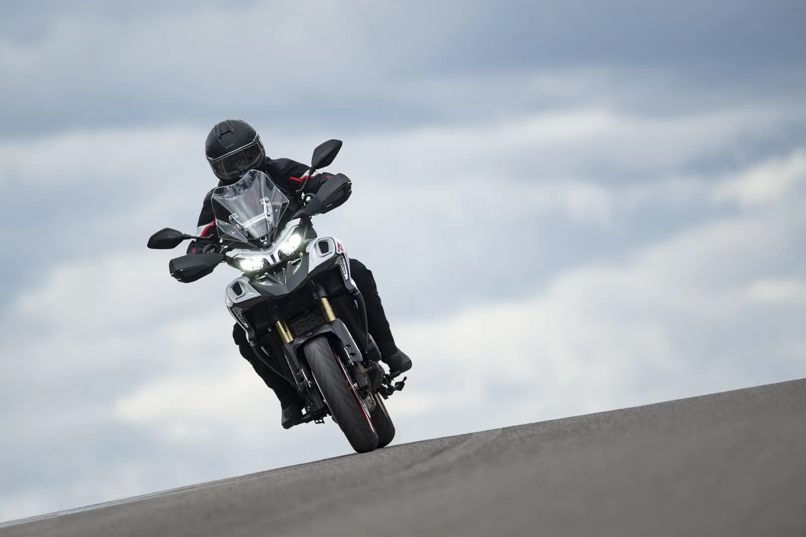 trk902stradale_action_14 - AutoBike Motorcyclist wearing helmet leaning into a curve on a sport bike on a sloped road under cloudy sky - AutoBike