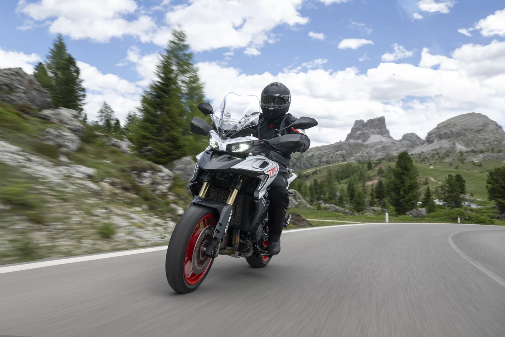 trk902stradale_action_3 - AutoBike Motorcyclist wearing helmet leans into a curved mountain road on a gray sport tourer with red wheels, scenic rocky hills in the background - AutoBike