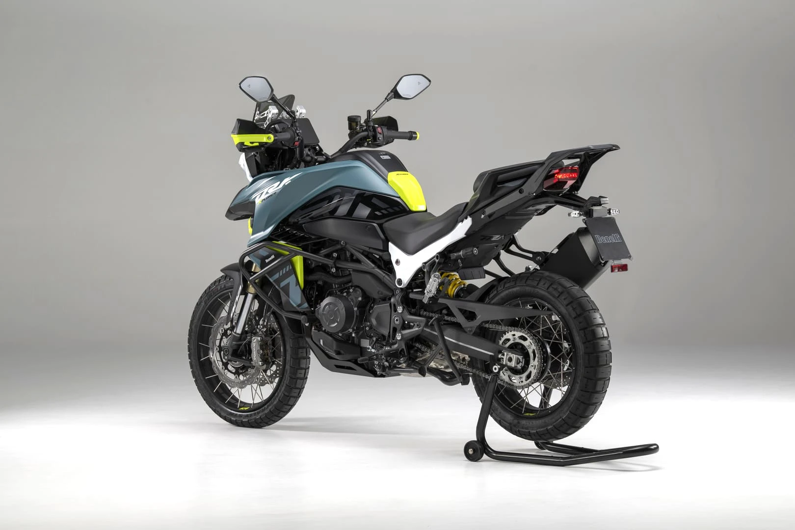 trk902xplorer_06 - AutoBike Side view of a Benelli adventure motorcycle on a paddock stand, blue-green body with neon-yellow accents in a studio setting - AutoBike