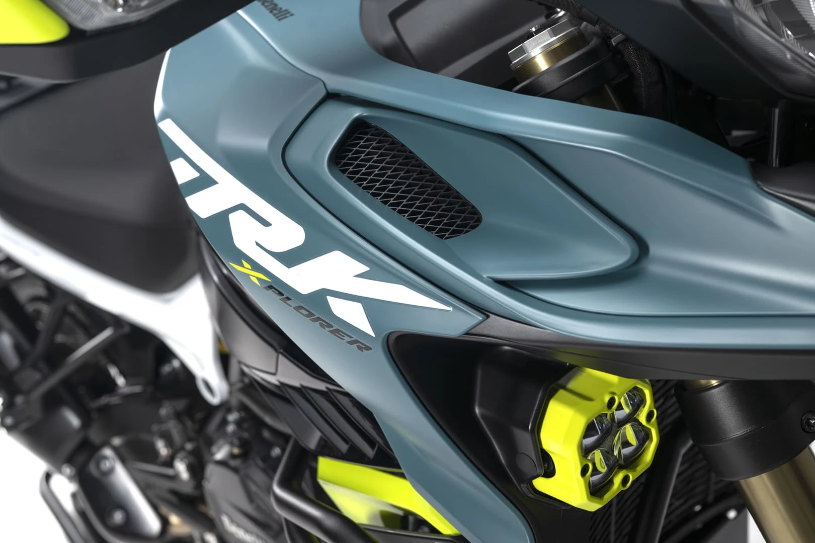 trk902xplorer_13 - AutoBike Close-up of a sport motorcycle's teal body panel with a black mesh vent and bright yellow-green suspension components visible. - AutoBike