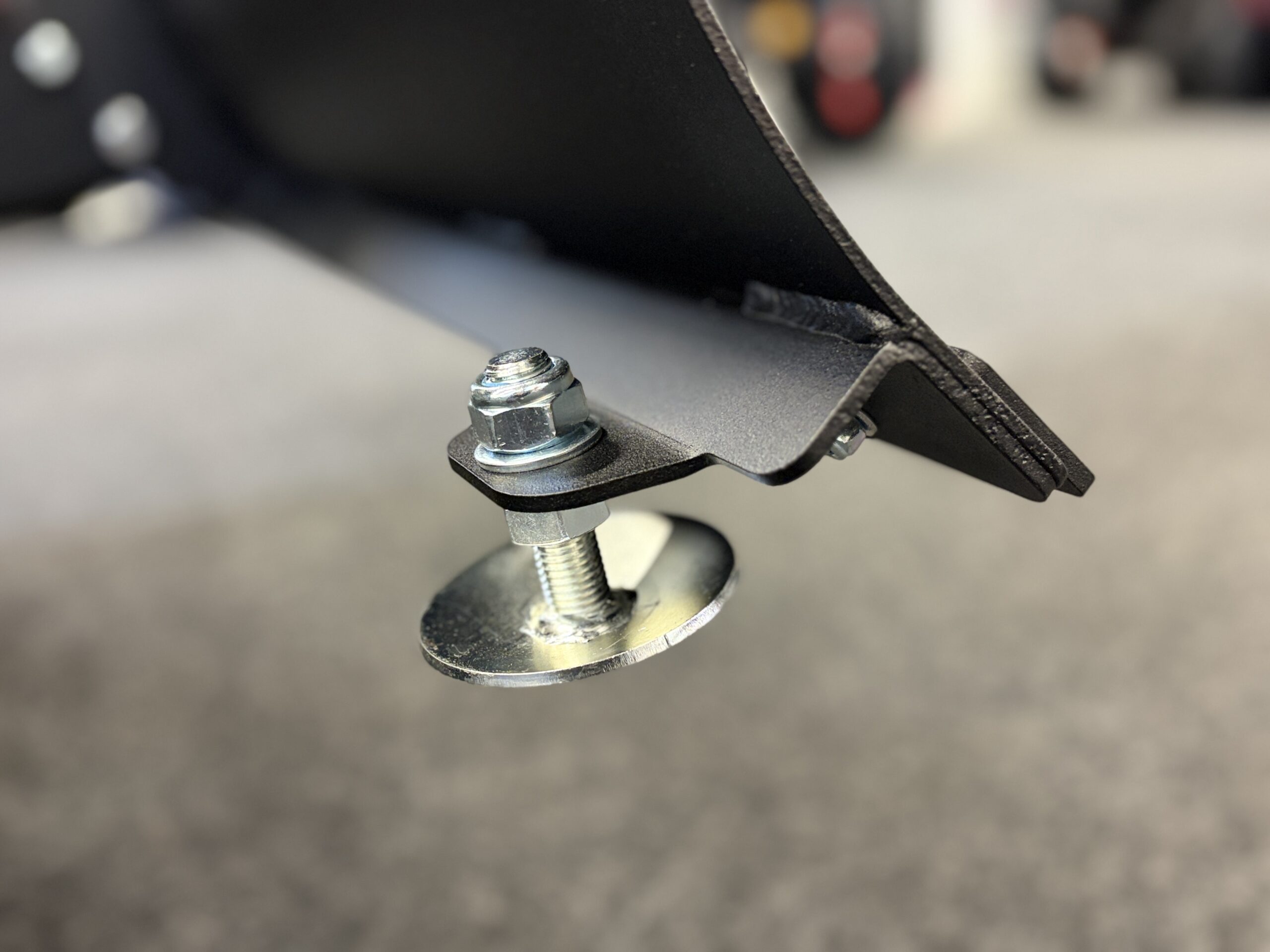 IMG_0472 - AutoBike Close-up of a bolt, nut and washer securing a black metal bracket to a frame, with a circular foot pad below. - AutoBike