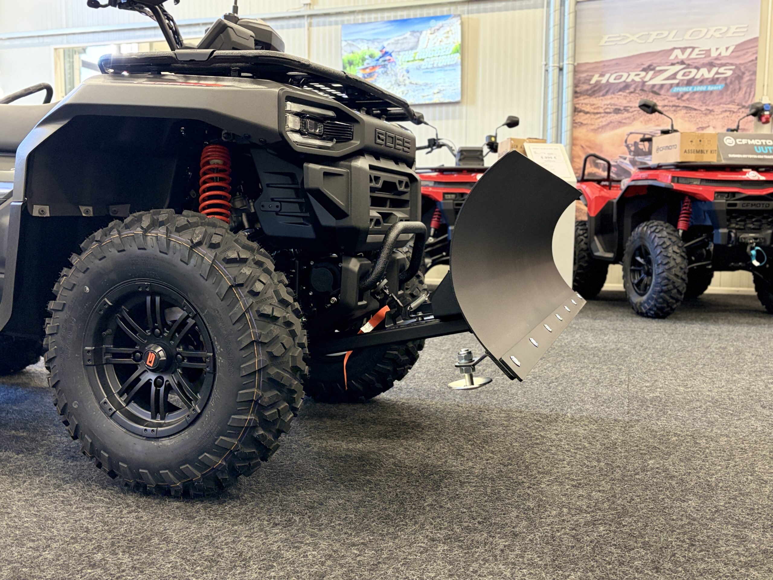 IMG_0476 - AutoBike Close-up of a black off-road ATV with a large knobby tire and red coil-spring suspension on display in a showroom. - AutoBike